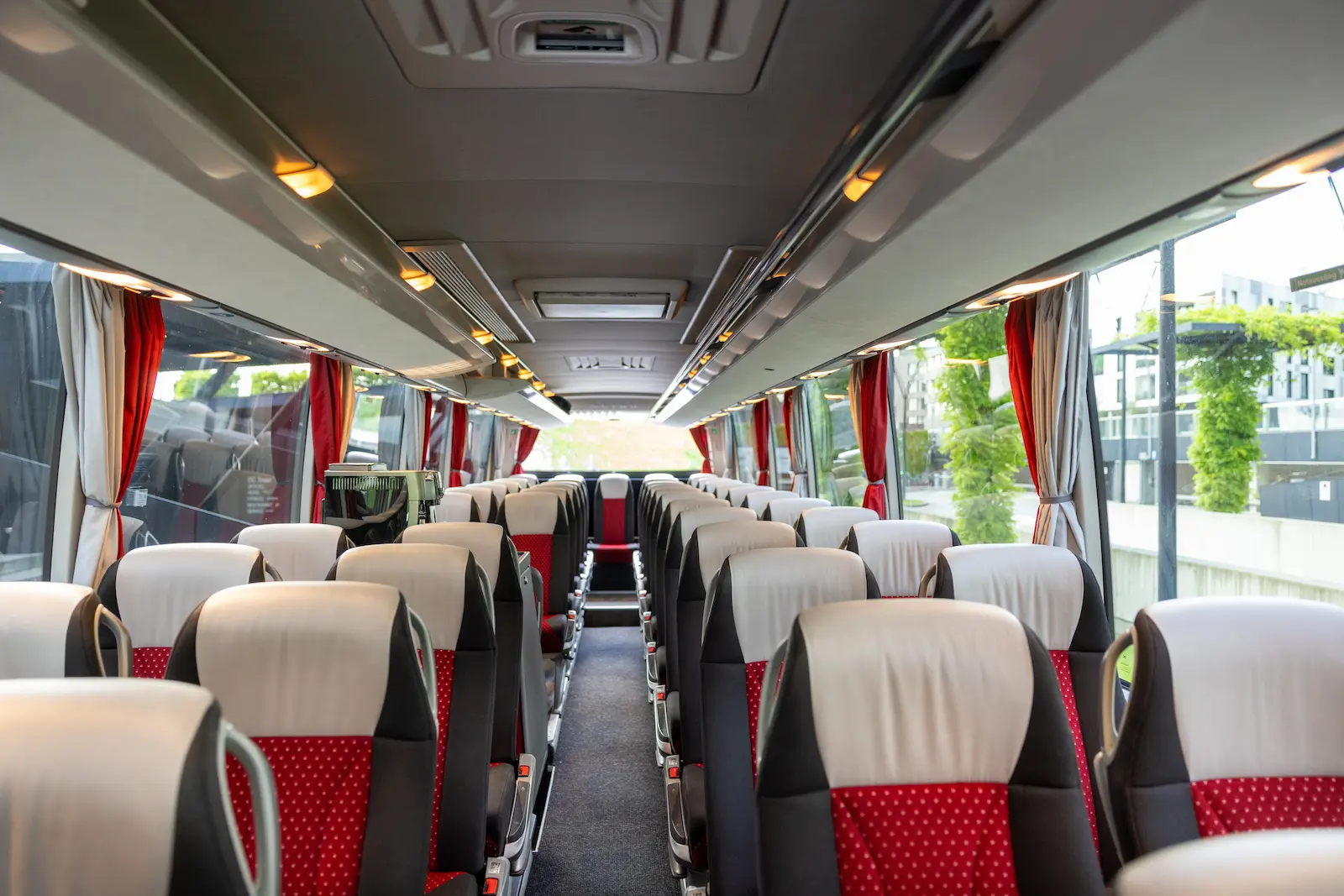 Setra Bus inside rear view displaying comfortable red and white seats with modern interior design, parked near a scenic urban area.