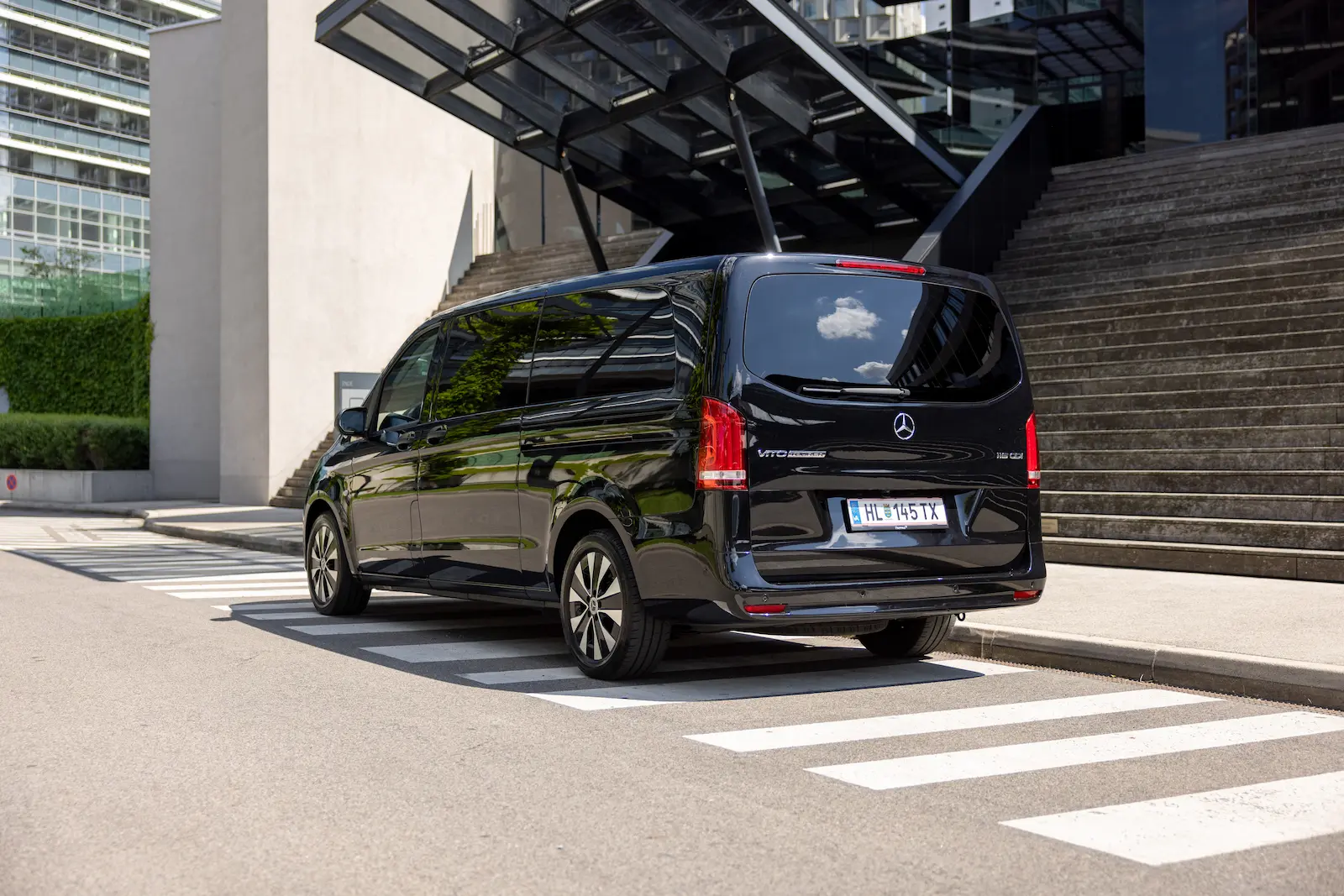 Stilvolle Mercedes-Benz Sprinter Rückansicht in Schwarz vor einer modernen Steintreppe mit eleganten Felgen.