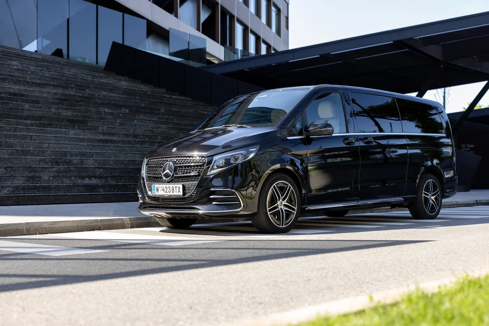 Ein eleganter Mercedes-Benz Vito Van steht vor einem modernen Bürogebäude mit Glasfassade und Treppen, perfekt für Geschäftszwecke.