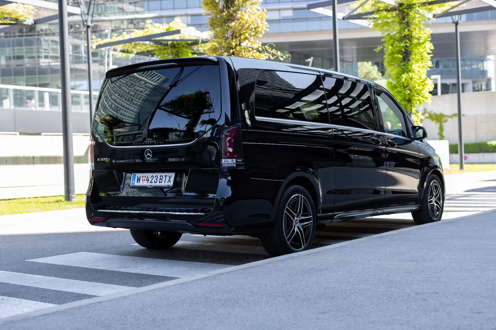 Mercedes Benz van rear view showcasing a sleek black design, parked near a modern building with a pedestrian crossing in the foreground.