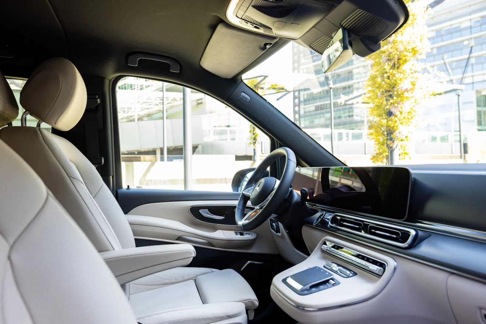Luxuriöser Mercedes-Benz Van Interior mit cremefarbenen Ledersitzen und modernem Armaturenbrett in urbaner Umgebung.