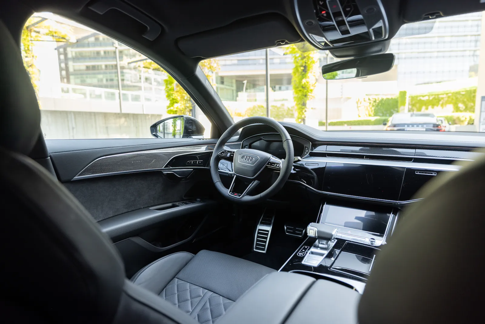 Moderne Audi A8 Long Innenansicht mit luxuriösen Ledersitzen und hochwertigem Armaturenbrett, geparkt vor einem urbanen Gebäude.