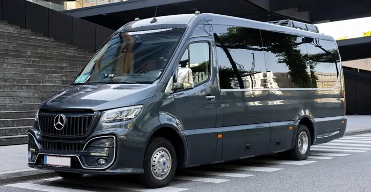 Ein eleganter MB Sprinter VIP Front View steht vor einem modernen Gebäude mit Treppen, ideal für luxuriöse Fahrten.